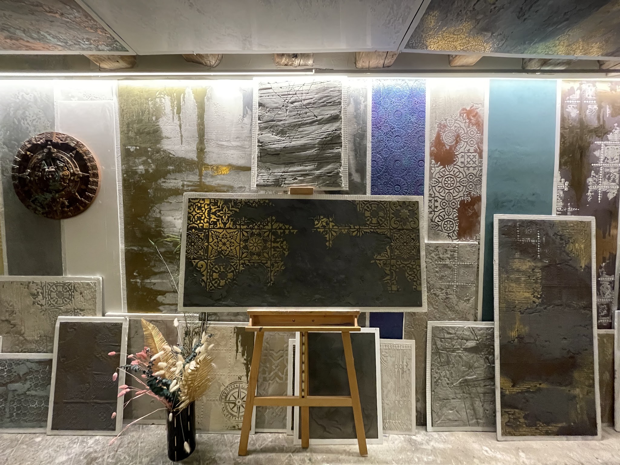 Atelierwand mit zahlreichen Muster- und Texturplatten in Gold, Blau und Stein-Optik